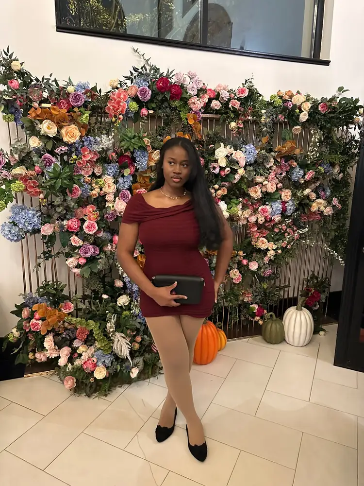 Aduwa in a burgundy dress by a floral wall